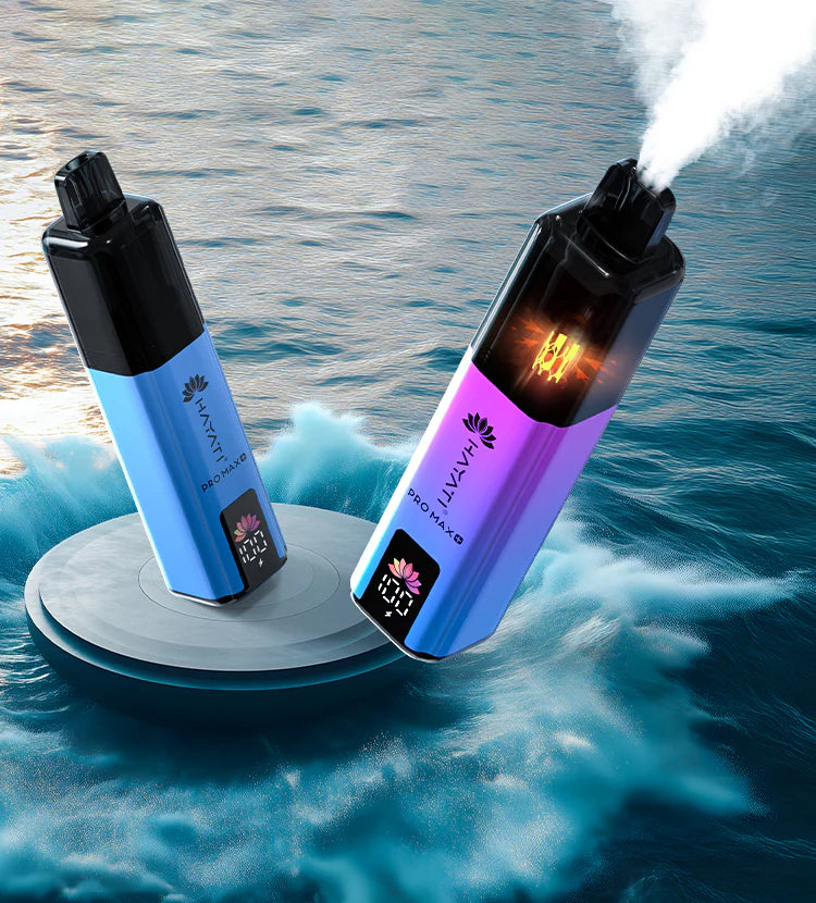 Hayati Pro Max Disposable Vapes – A promotional lifestyle image showing two different colored Hayati Pro Max vapes set against a dramatic ocean background, with one actively firing and emitting vapor.
